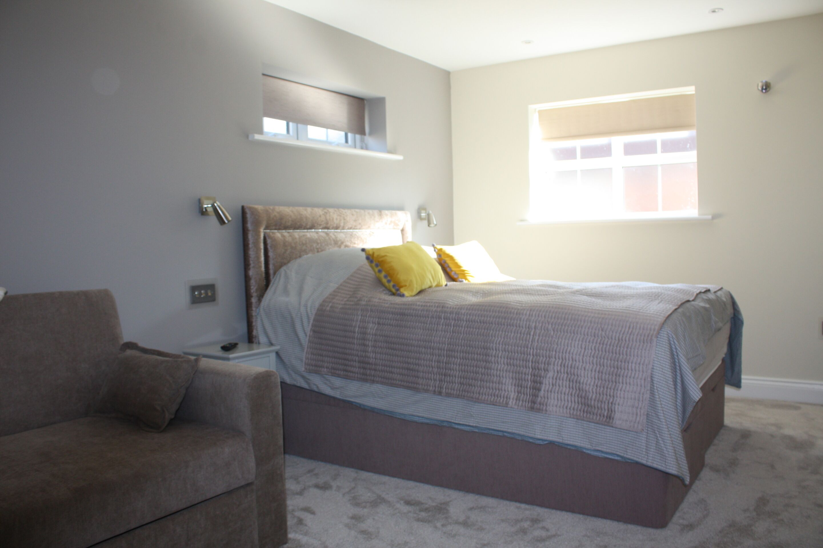A bedroom with a bed, a nightstand, a lamp, a window, and a couch.