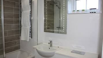 Un baño con bañera, lavamanos, espejo con iluminación y ventana con plantas.