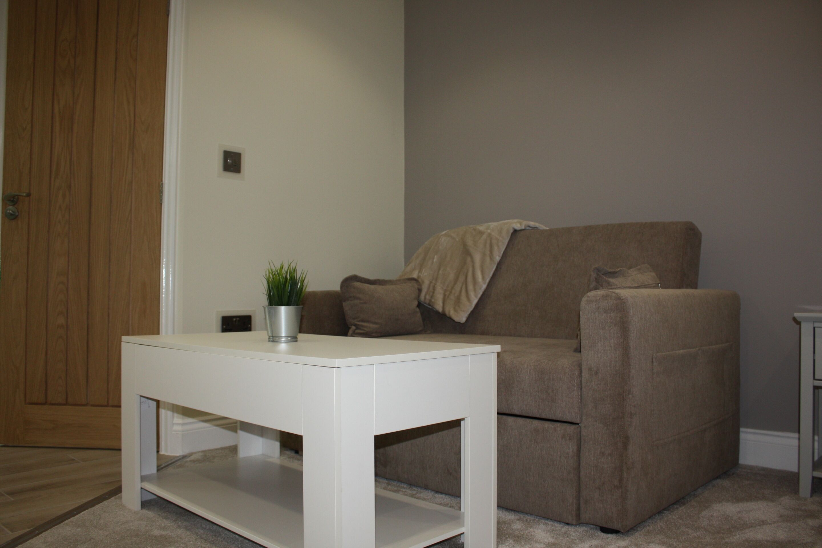 A living room with a white coffee table, a brown sofa, and a wooden door.