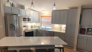 A modern kitchen with grey cabinets, a stainless steel refrigerator, a microwave, and a large island with bar stools. - Luxury WATERFRONT home with HEATED POOL AND SPA Sleeps 28+ (Kingsland)