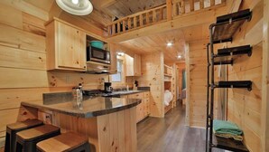 L’intérieur d’une cabane en bois comprend un coin cuisine, des tabourets de bar, un four à micro-ondes et un porte-objets suspendu.
