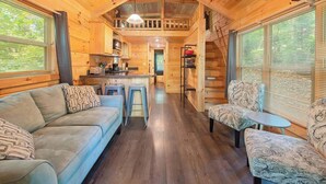 L’intérieur d’une cabane en rondins, avec un canapé, des fauteuils, une table à manger et un coin cuisine.
