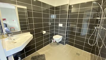 A modern bathroom with black tiles, a white sink, a toilet, and a shower area.