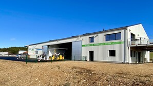 Een groot industrieel gebouw met een bord waarop staat: Baptême de L'Air - Boissons Glaces - Boutique - Accueil.