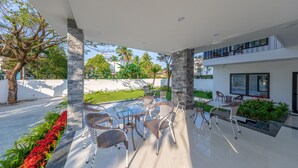 An outdoor patio with modern wicker furniture, a glass table, and a view of a lush garden and palm trees. - Bespoke Villa Hoi An (Da Nang)