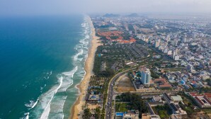 An aerial view of a coastal city with a beach, residential areas, and a mix of modern and traditional buildings. - Bespoke Villa Hoi An (Da Nang)