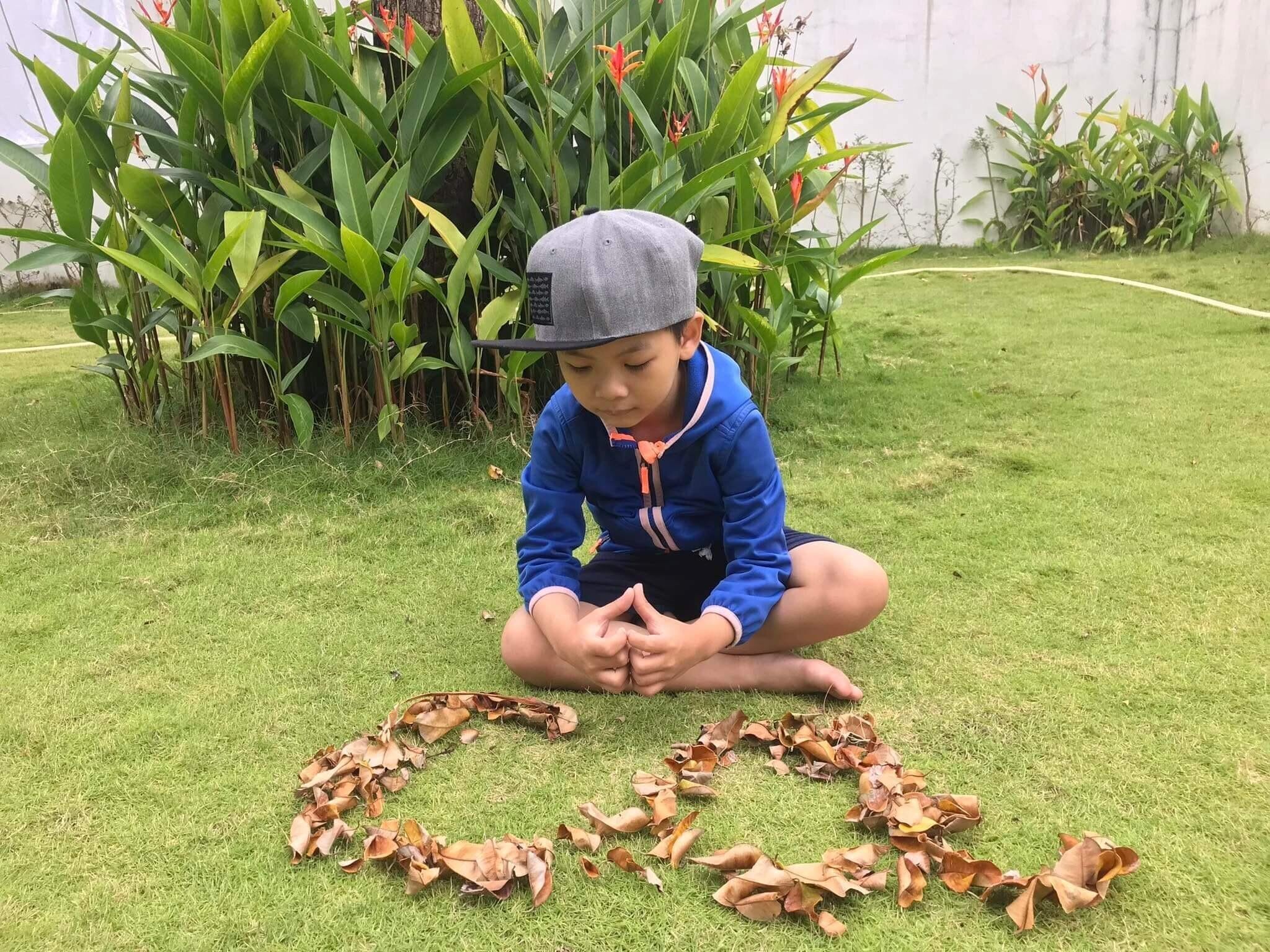 Niño sentado sobre la hierba, rodeado de hojas en círculo.