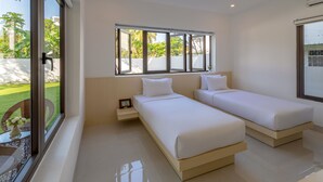 A modern hotel room with two single beds, a large window with a view of greenery, and a small table with a vase. - Bespoke Villa Hoi An (Da Nang)