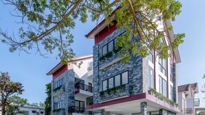 A modern multi-story building with a spacious outdoor patio, a staircase leading to the entrance, and a well-maintained lawn. - Bespoke Villa Hoi An (Da Nang)