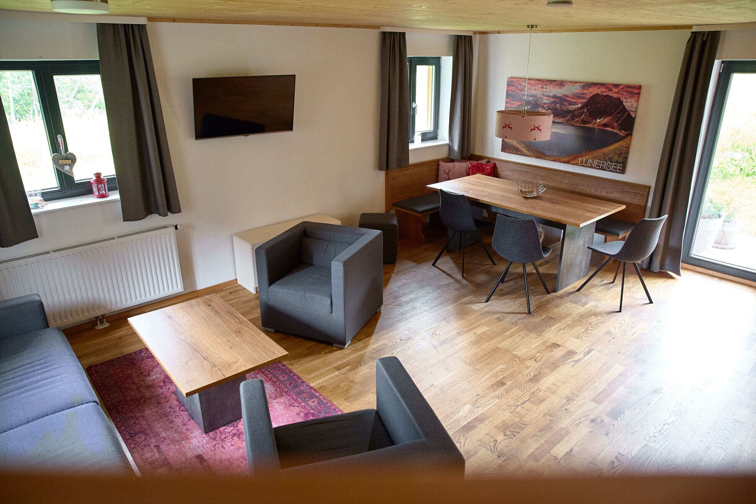 A modern living room with a sofa, a coffee table, a dining table with chairs, and a TV mounted on the wall.