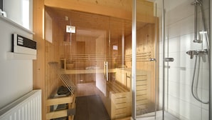 A modern sauna with glass doors, a wooden interior, and a separate shower area. - 4513 Alpin 13 (St. Gallenkirch)