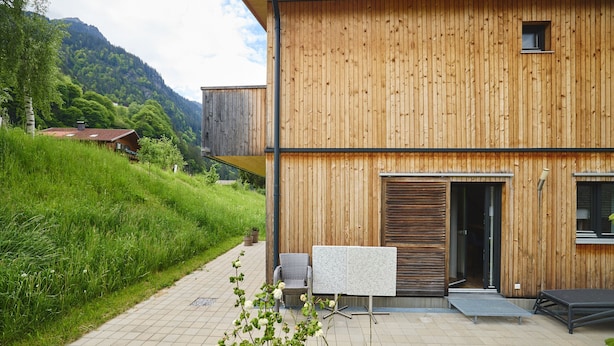 A wooden building with a paved patio, a chair, a table, and a small garden area. - 4513 Alpin 13 (St. Gallenkirch)