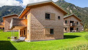 Een modern houten huis met een balkon, een gazon en een bergachtige achtergrond.