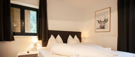 A hotel room with a bed, a nightstand, a lamp, a window with curtains, and a framed picture on the wall.