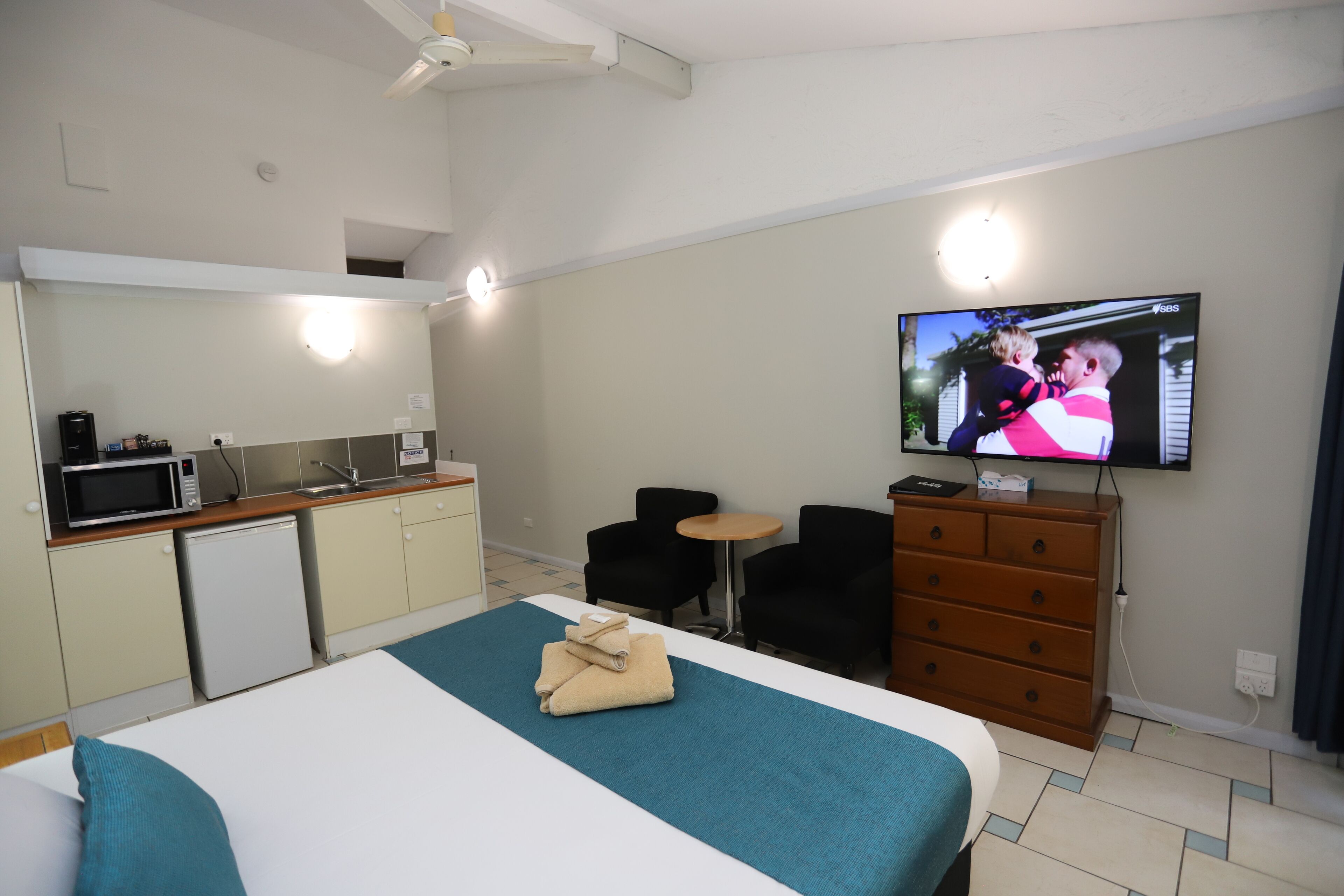 A hotel room with a bed, a TV, a small kitchenette, and a seating area.