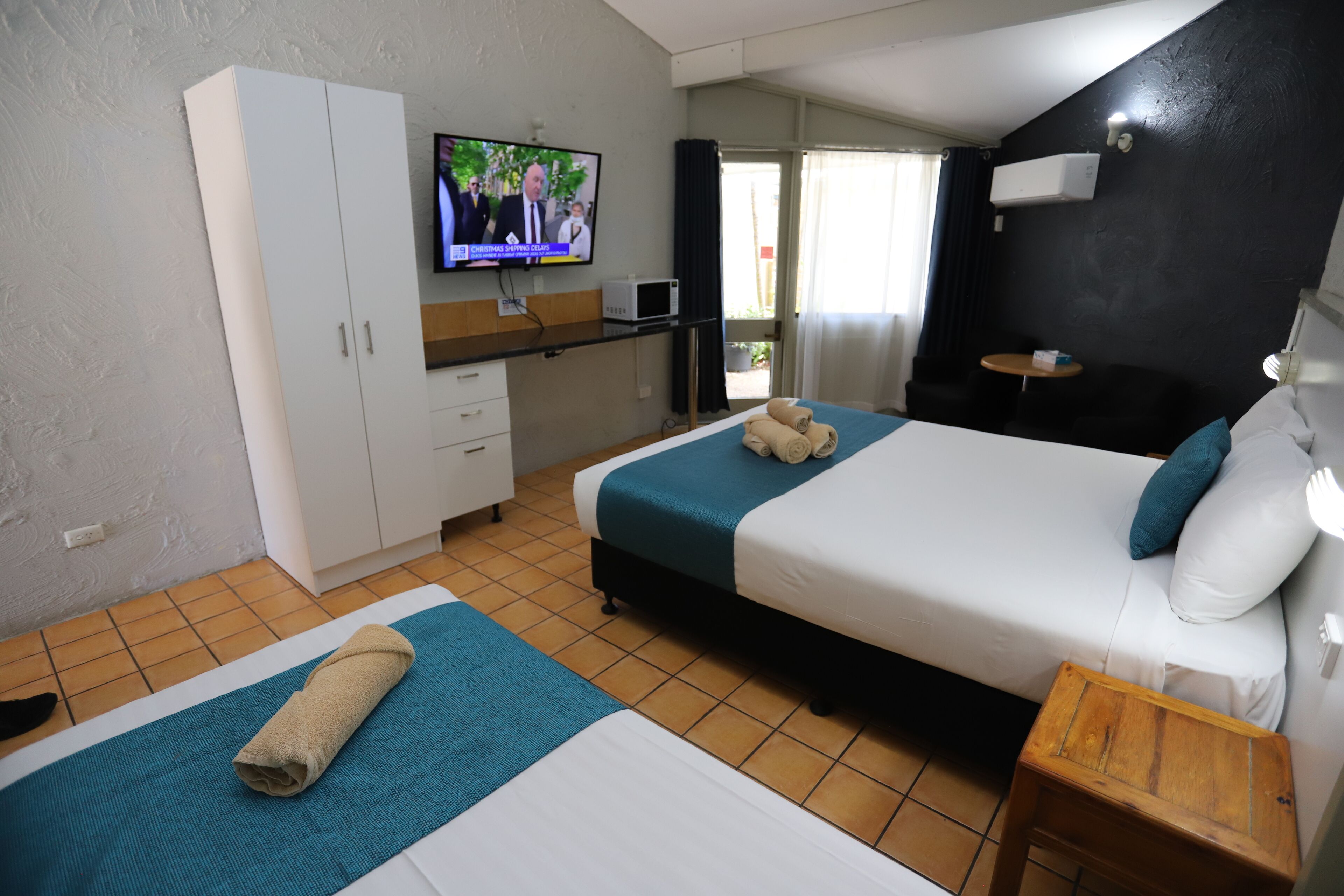 A hotel room with two beds, a television, a small table, and a wardrobe.