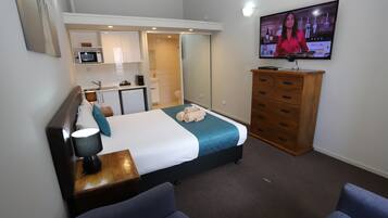 A hotel room with a bed, a TV, a desk, a chair, a dresser, and a kitchenette.