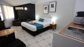 Een hotelkamer met een bed, nachtkastje, lamp en een kitchenette.