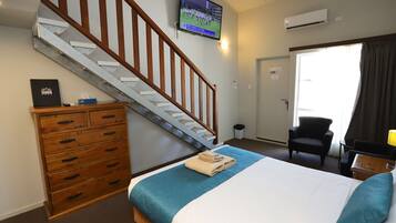 A hotel room with a bed, wooden dresser, a TV on the wall, a staircase, and a door leading outside.