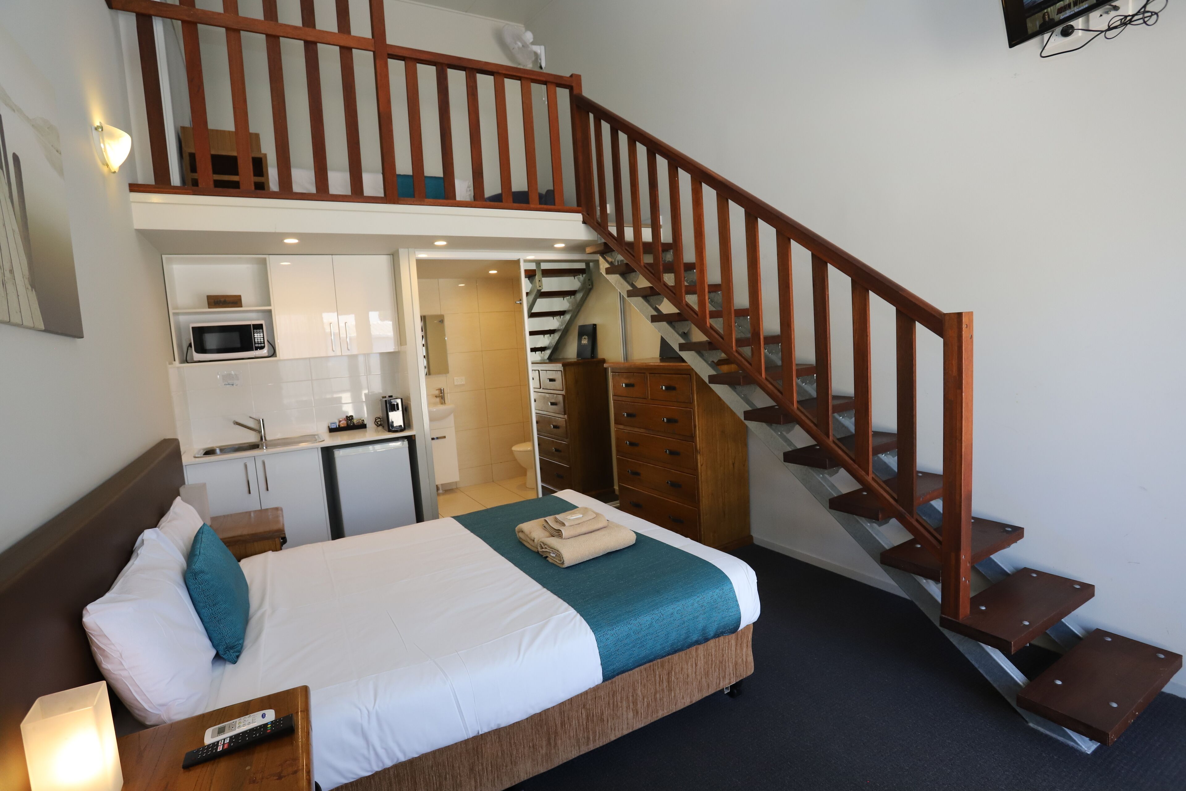 Una habitación de hotel con cama, escritorio, microondas, armario y una escalera.