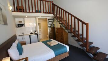A hotel room with a bed, a desk, a microwave, a wardrobe, and a staircase.