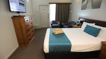 Quarto de hotel com uma cama, cómoda de madeira, televisão, cadeira e um quadro na parede.