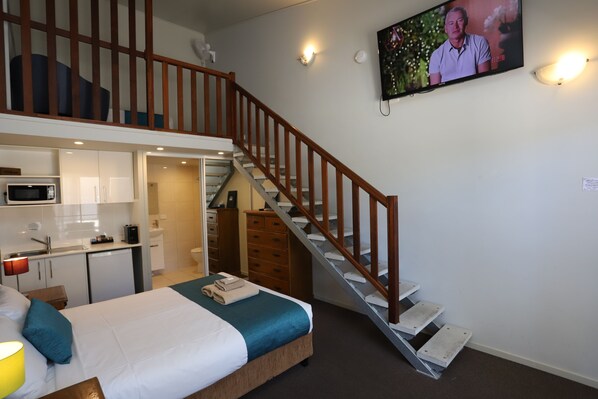 A hotel room with a bed, a wooden staircase, a television, and a kitchenette. - Kallangur North Lakes Motel (Kallangur)