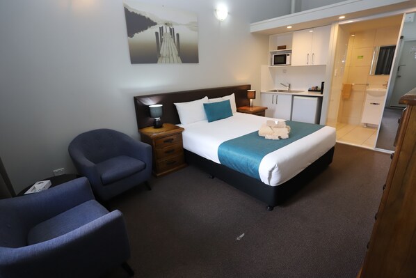 A hotel room with a bed, a desk, a chair, a painting, and a kitchenette.