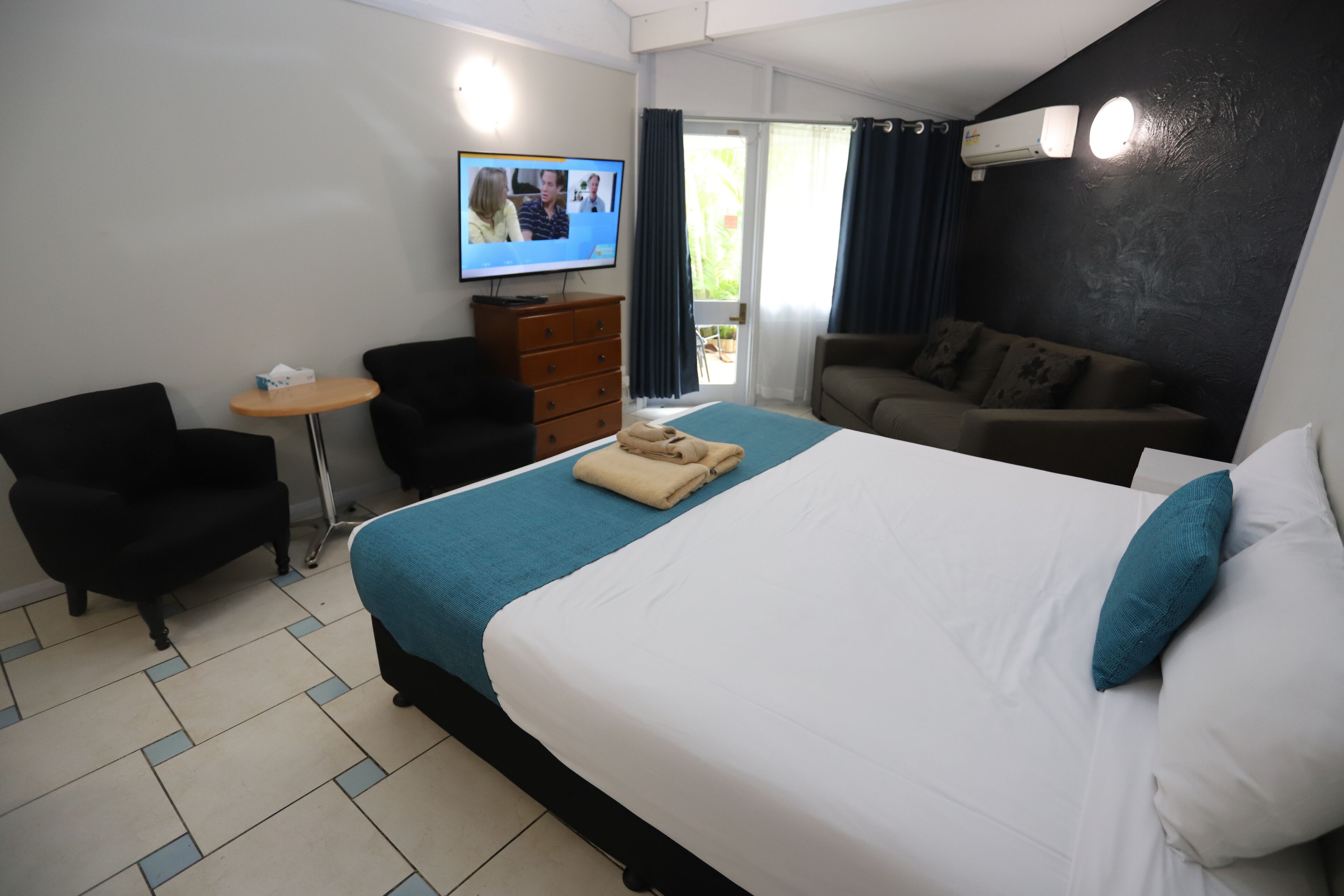 Une chambre d’hôtel équipée d’un lit, d’un bureau, d’une chaise, d’un canapé et d’un téléviseur affichant une communication vidéo.