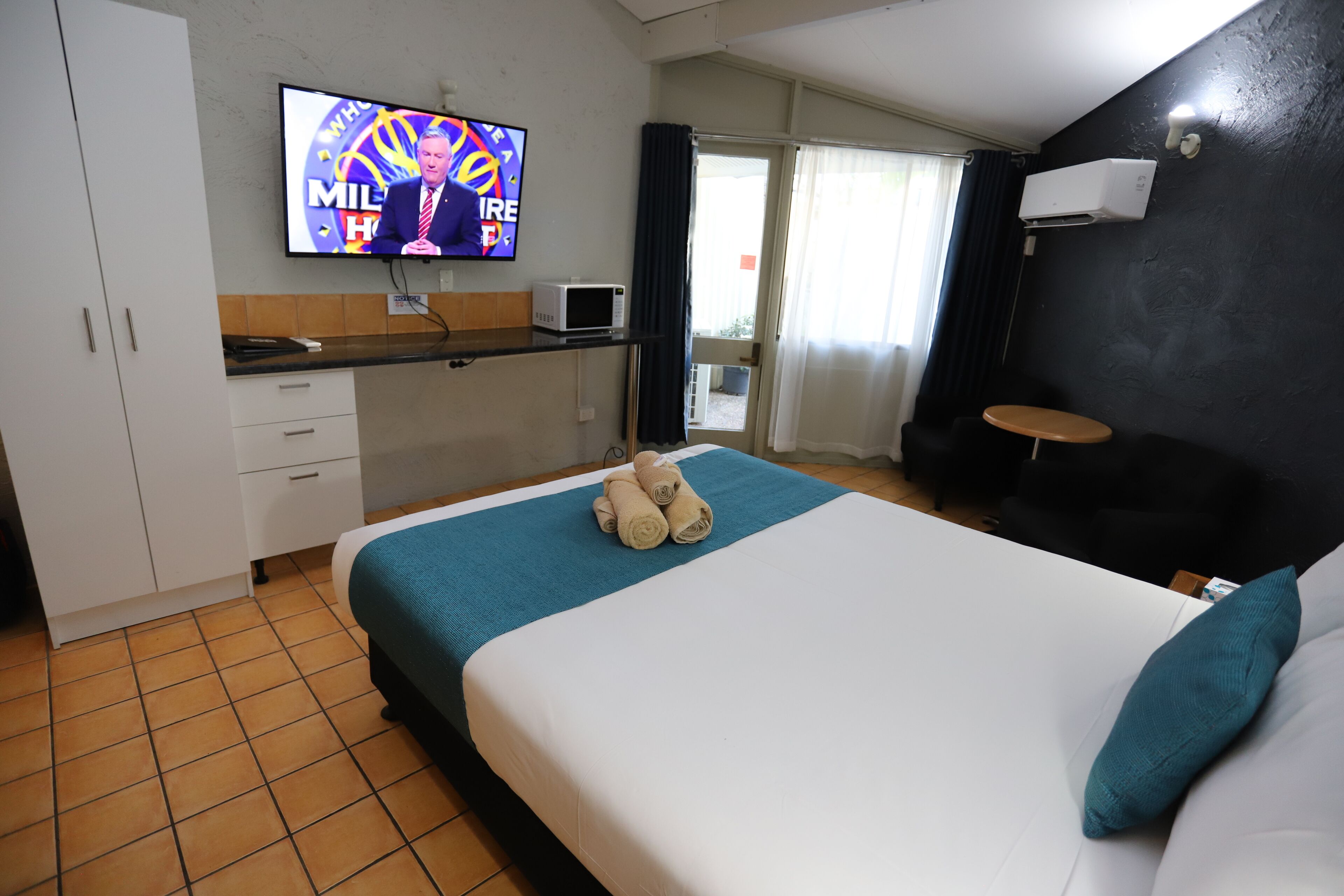 A hotel room with a bed, a television, a microwave, and a small table.