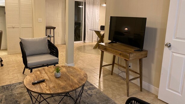 A living room with a sofa, a coffee table, a TV on a wooden stand, and a sliding glass door leading to another room.