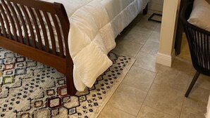 A neatly made bed with a wooden headboard, two bedside tables with lamps, and a patterned rug on a tiled floor.