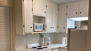 A compact kitchen with white cabinets, a stove, a microwave, and a refrigerator.