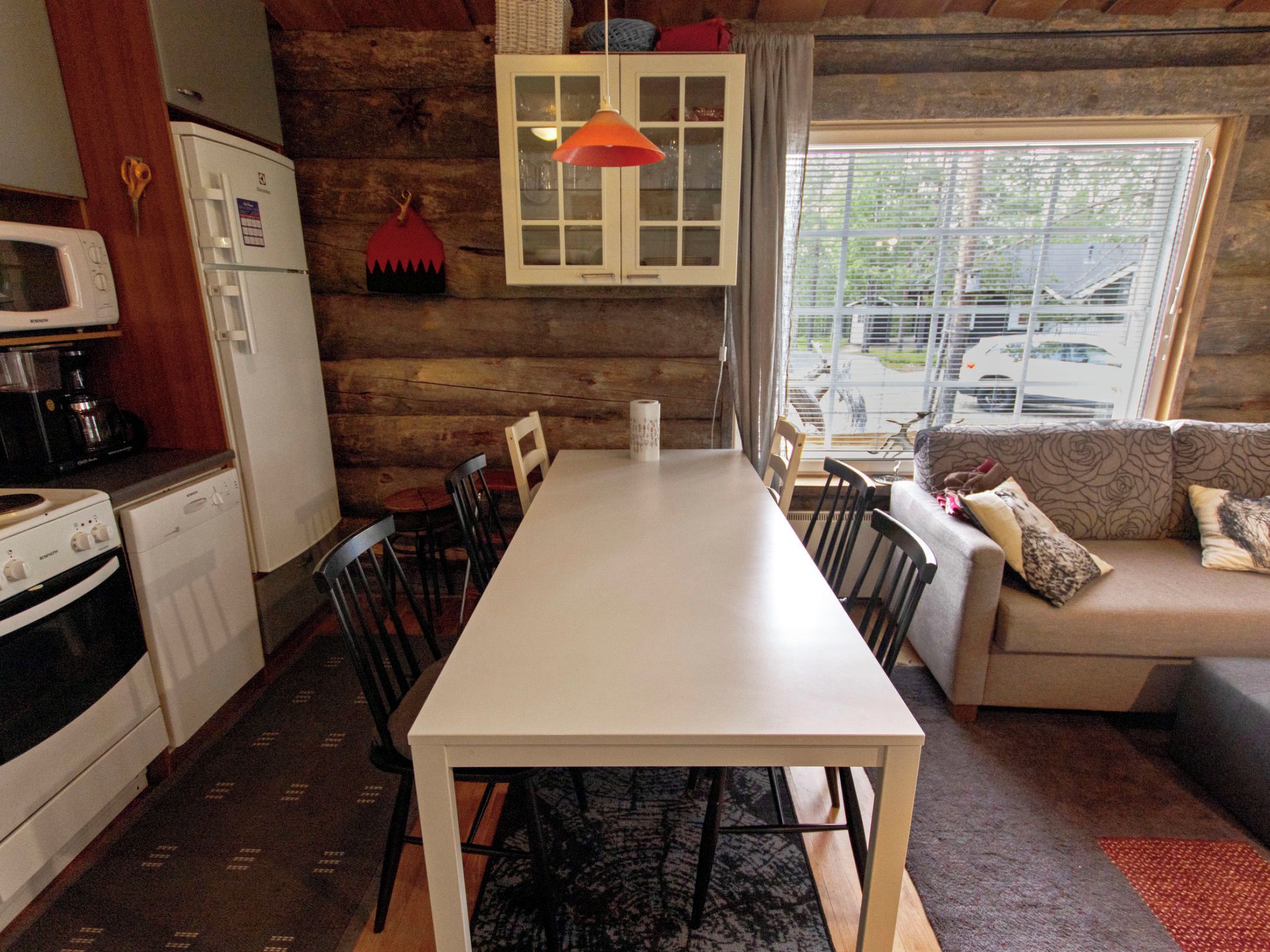 A compact kitchen with a dining table and chairs, a sofa, and a window with a view of the street.