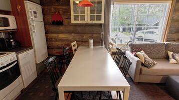 A compact kitchen with a dining table and chairs, a sofa, and a window with a view of the street.