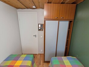 Ein kleines Zimmer mit einem Holzschrank, einer weißen Tür und zwei Betten mit bunter Bettwäsche.
