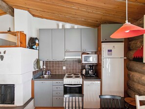 Une cuisine compacte équipée d’une cuisinière, d’un four à micro-ondes et d’un réfrigérateur, avec des poutres en bois apparentes au plafond et une esthétique rustique.