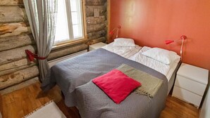 A log cabin bedroom with a bed, a nightstand, a window with curtains, and a red lamp. - Hankipolku 7b / ukuli by Interhome (Ylläsjärvi)