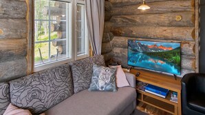 A cozy log cabin room with a sofa, a television displaying a scenic landscape, and a window with blinds. - Hankipolku 7b / ukuli by Interhome (Ylläsjärvi)