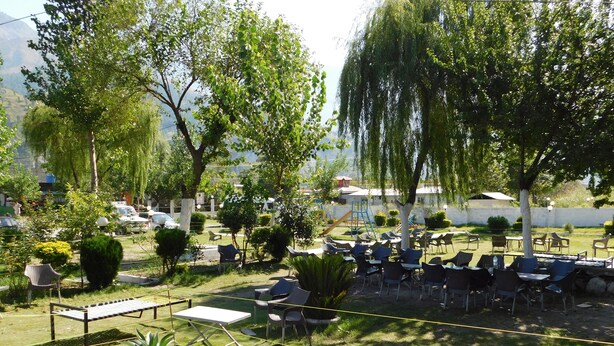 An outdoor seating area with tables and chairs, surrounded by trees and greenery. - Pine View hotel and Restaurant (Balakot)