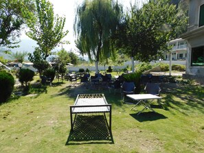 An outdoor seating area with tables and chairs, surrounded by trees and a view of the sea.