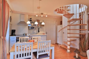 A kitchen with white cabinets, a wooden dining table, and a spiral staircase. - Landhaus Victoria, Seestern (Ostseebad Boltenhagen)