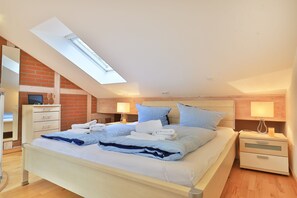 Un dormitorio con tragaluz, una cama con ropa de cama azul, dos mesitas de noche y un aparador de madera.