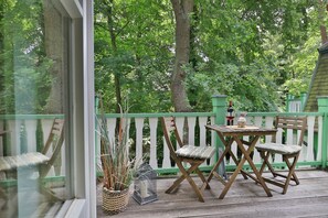 Une terrasse en bois avec une table et des chaises, entourée d’une clôture verte et d’arbres.