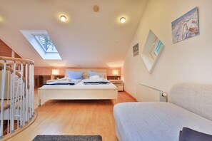 A bedroom with a skylight, a bed, a nightstand, a sofa, and a staircase.