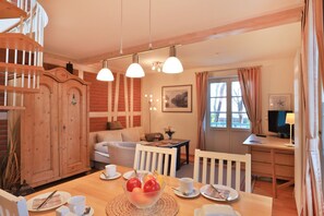 Una habitación acogedora con una mesa de comedor de madera, sillas, un sofá, un televisor y una escalera.