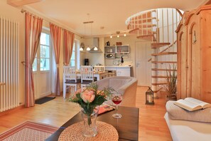A cozy living room with a sofa, a coffee table with a vase of flowers, a dining area with chairs, and a kitchen in the background.
