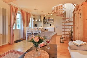 A cozy living room with a sofa, a coffee table with a vase of flowers, a dining area with chairs, and a kitchen in the background. - Landhaus Victoria, Seestern (Ostseebad Boltenhagen)