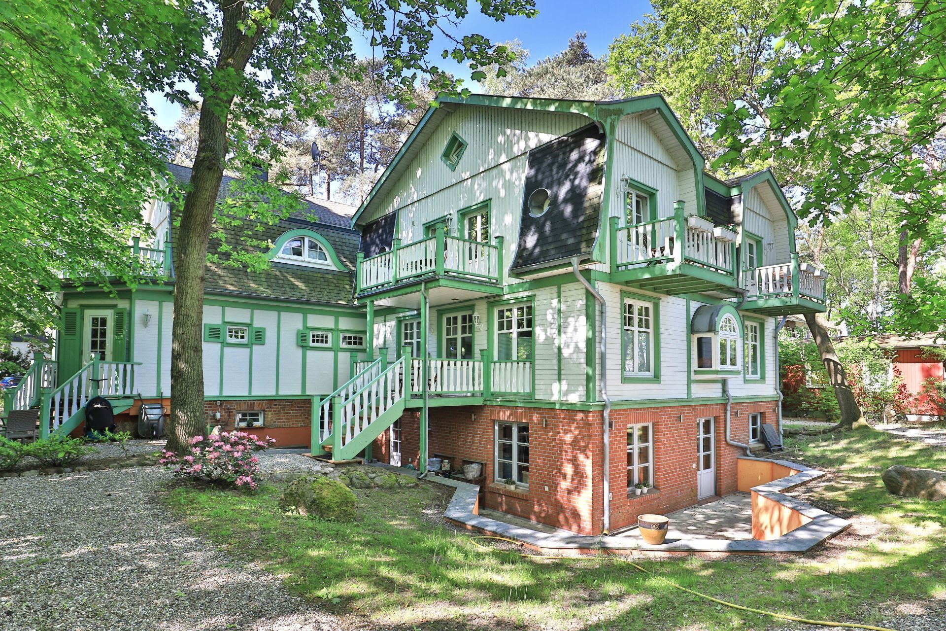 Ein mehrstöckiges Haus mit grün-weißer Fassade, einem Balkon und einem Garten.