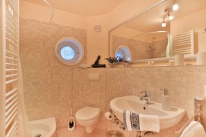 Un baño con bañera, inodoro, lavamanos y un ventanal redondo.